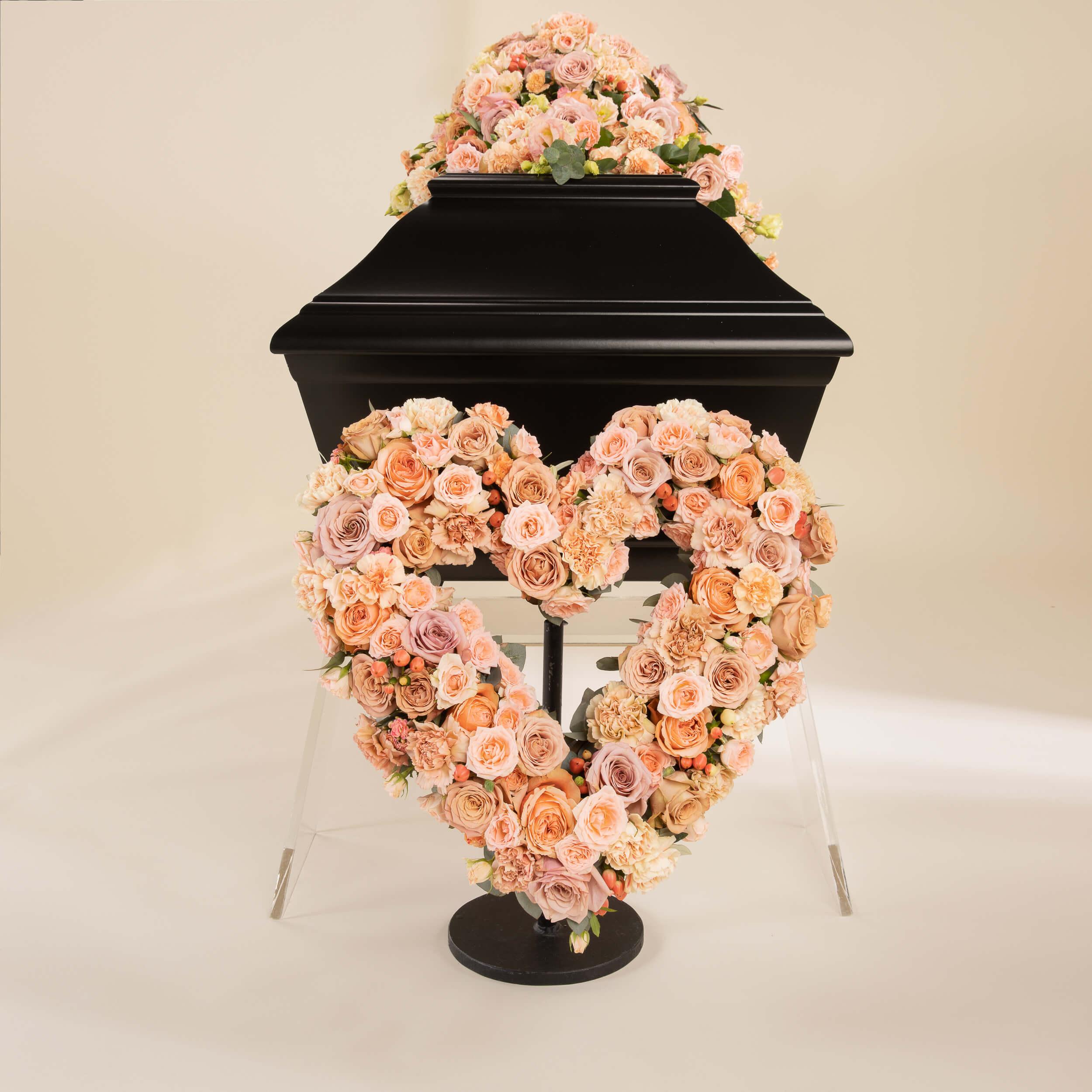 Et hjerte med duse lys-rosa farger foran en sort kiste med båredekorasjon i matchende farger.