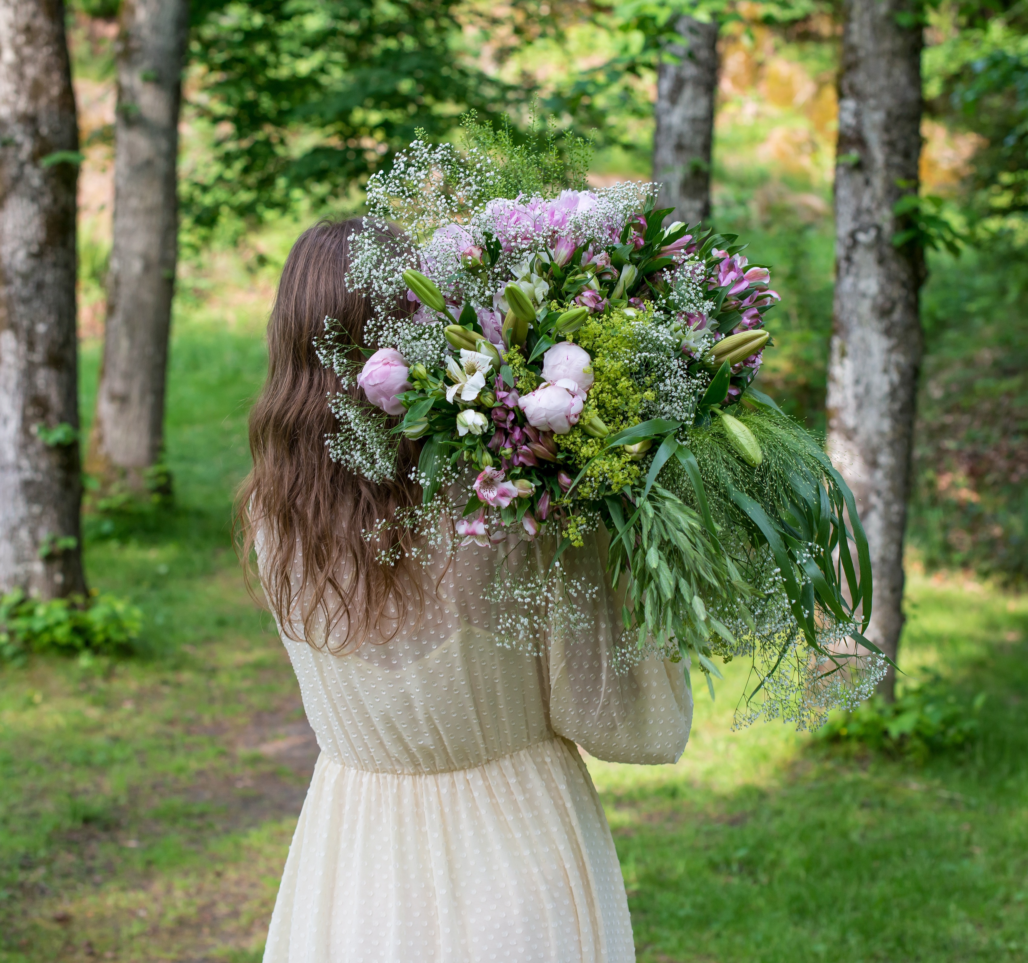 En bukett med peoner, alstroemeria, brudeslør og strå som holdes over skulderen.